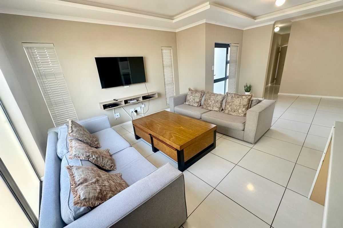 A bright and spacious living room featuring neutral walls, tiled flooring, recessed ceiling details, and a floating media shelf.