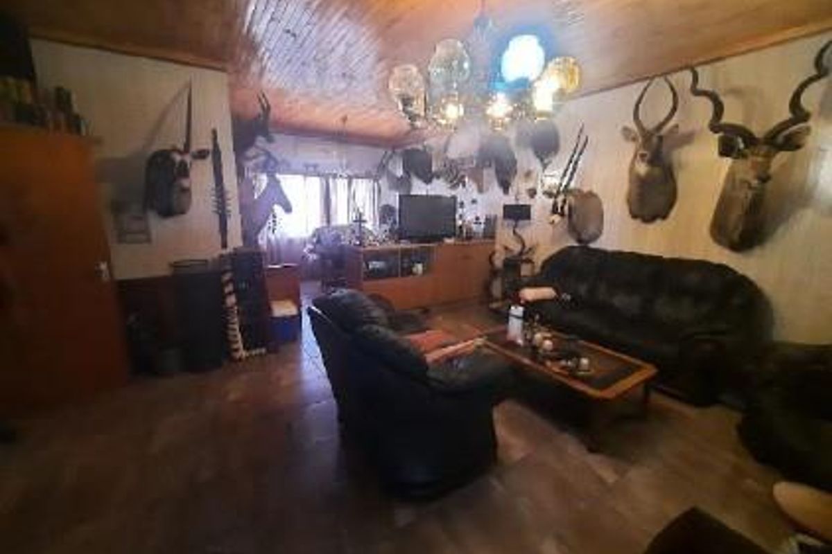 A spacious living room featuring a wooden tongue-and-groove ceiling, tiled flooring, and a central chandelier, providing a rustic atmosphere.