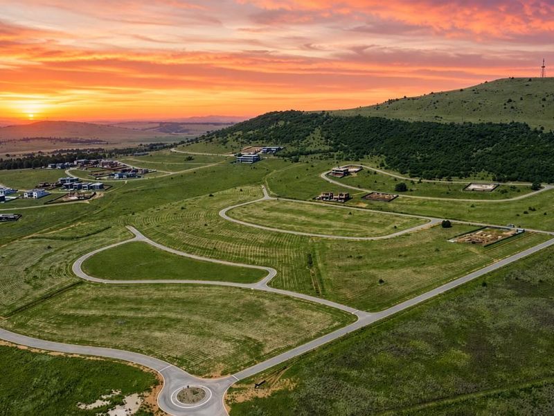 Aerial view of a residential development estate featuring paved roads, a roundabout, and vacant plots set against a scenic sunset landscape.