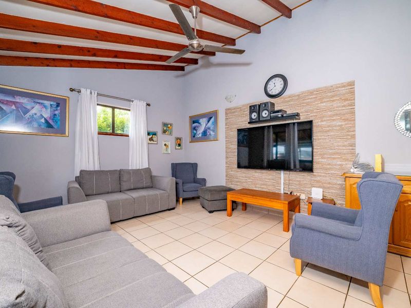 Spacious living room featuring exposed timber ceiling beams, a ceiling fan, tiled flooring, and a decorative stone-look feature wall.
