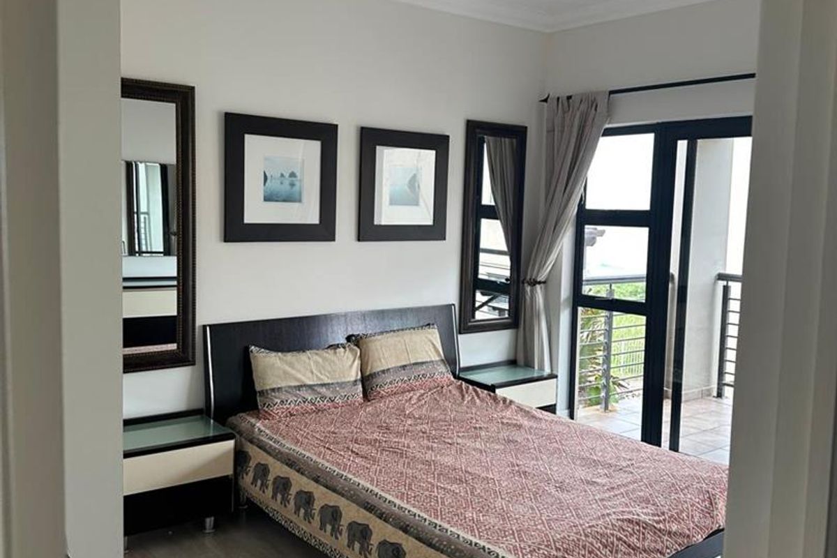 A well-maintained bedroom featuring laminate flooring, neutral walls, and a sliding glass door providing access to an outdoor balcony area.