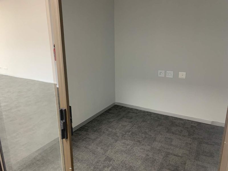 A clean, empty office space featuring grey carpet tiles, neutral walls, and a sliding glass door entry with integrated electrical and data points.