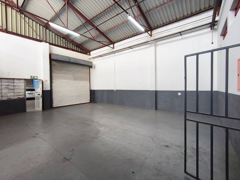 Spacious industrial utility space featuring high ceilings with exposed steel trusses, concrete flooring, and a large roller shutter door for easy access.