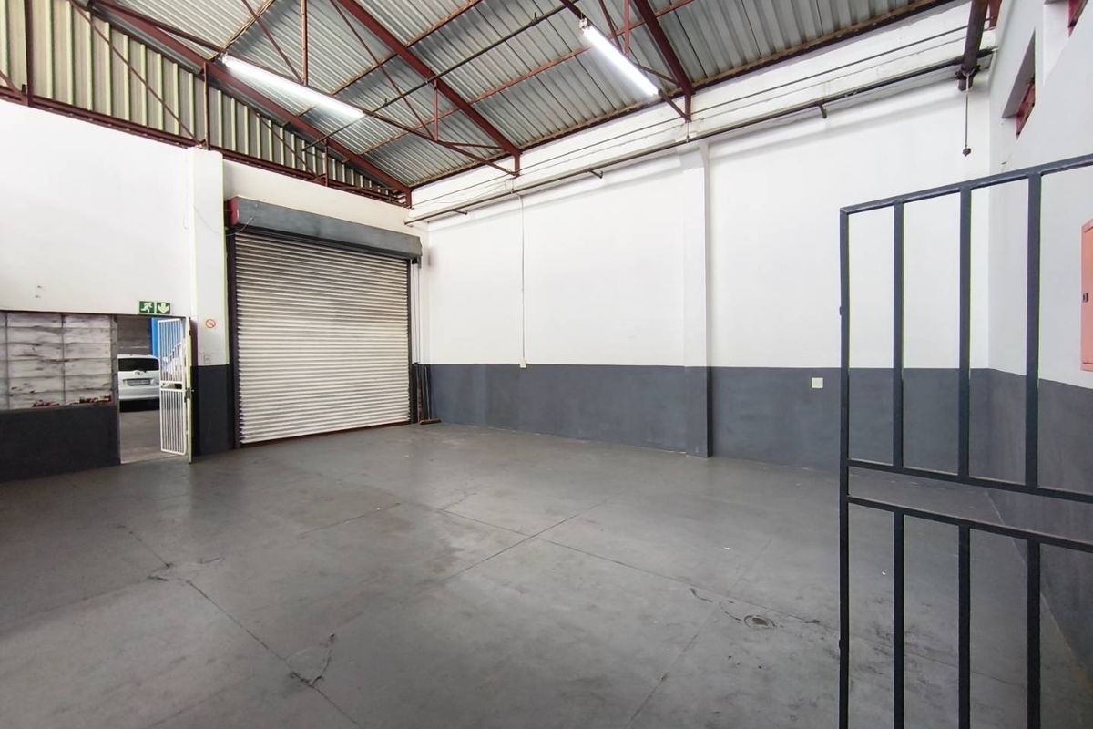 Spacious industrial utility space featuring high ceilings with exposed steel trusses, concrete flooring, and a large roller shutter door for easy access.