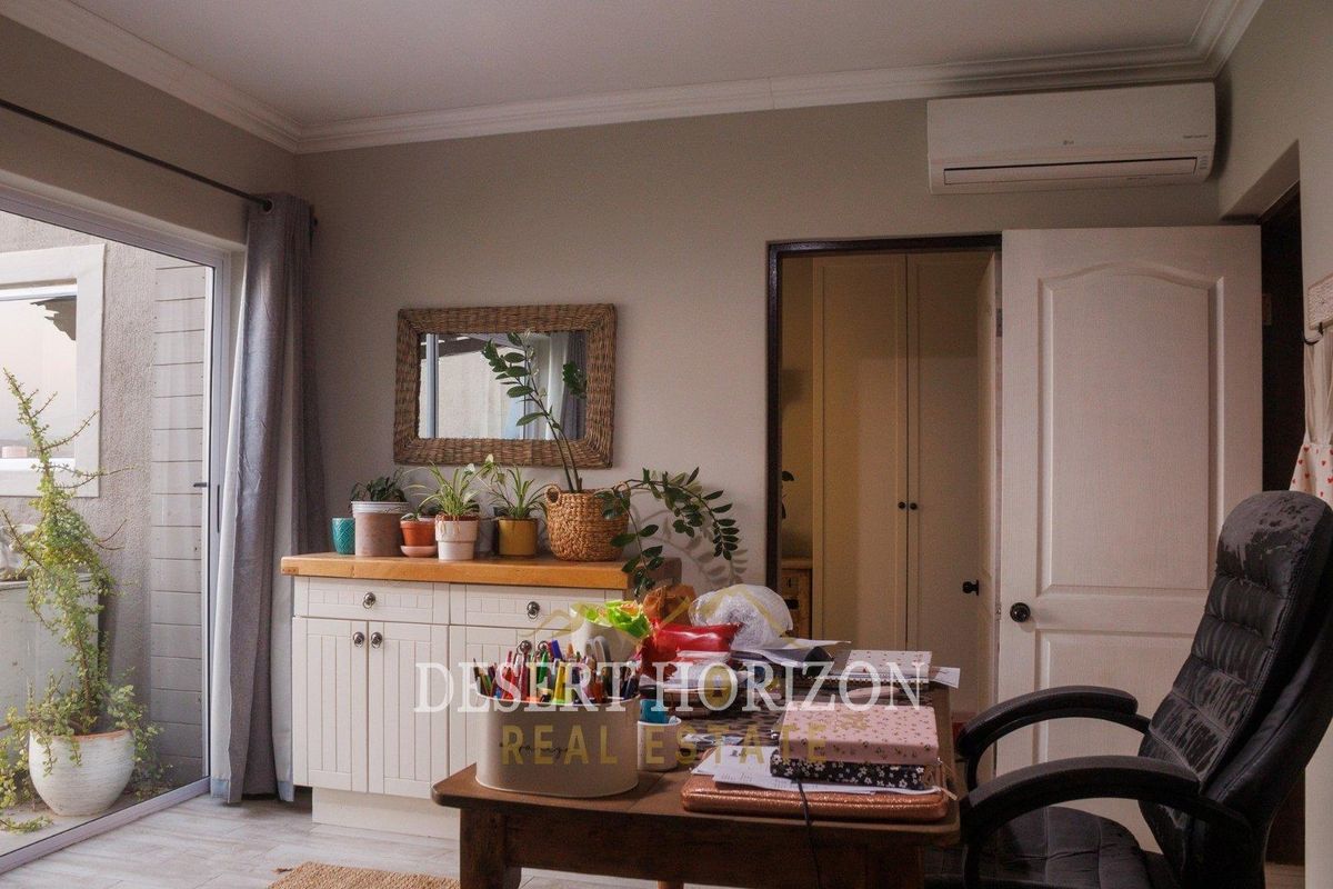A functional bedroom or home office space featuring built-in cabinetry, a wall-mounted air conditioning unit, and sliding glass doors leading to an outdoor area.