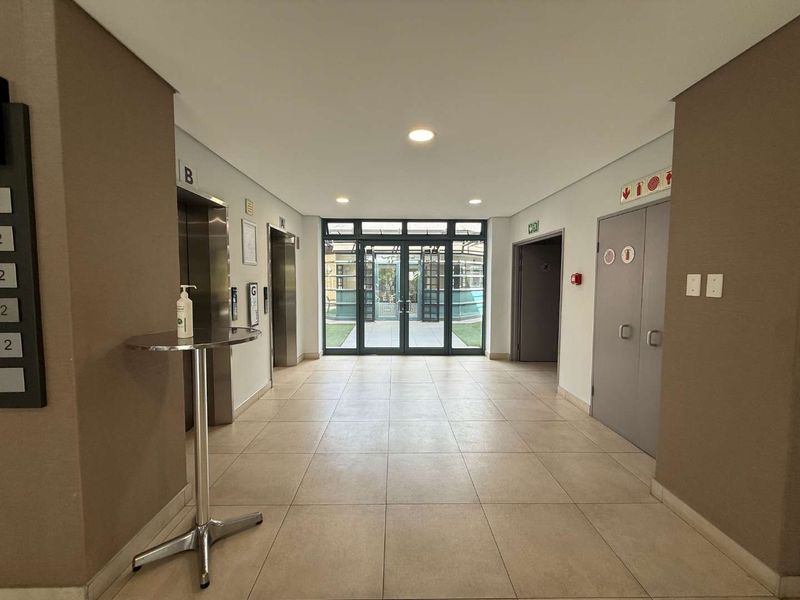 A clean and well-maintained commercial building lobby featuring tiled flooring, elevator access, and glass entrance doors leading to an outdoor area.