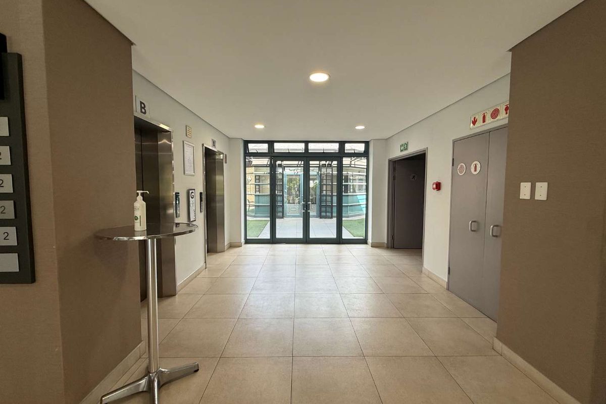 A clean and well-maintained commercial building lobby featuring tiled flooring, elevator access, and glass entrance doors leading to an outdoor area.