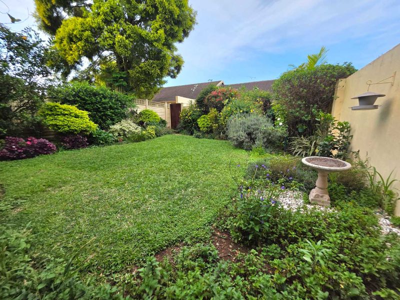 A well-maintained private garden featuring a lush green lawn, established shrubbery, and secure boundary walls.
