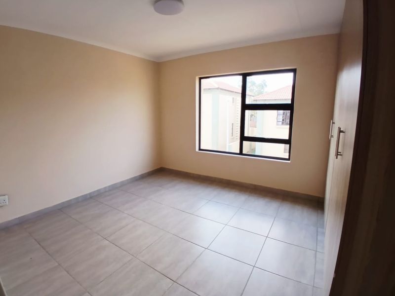 A clean, empty bedroom featuring neutral wall paint, tiled flooring, and built-in cupboards, offering a blank canvas for personalization.