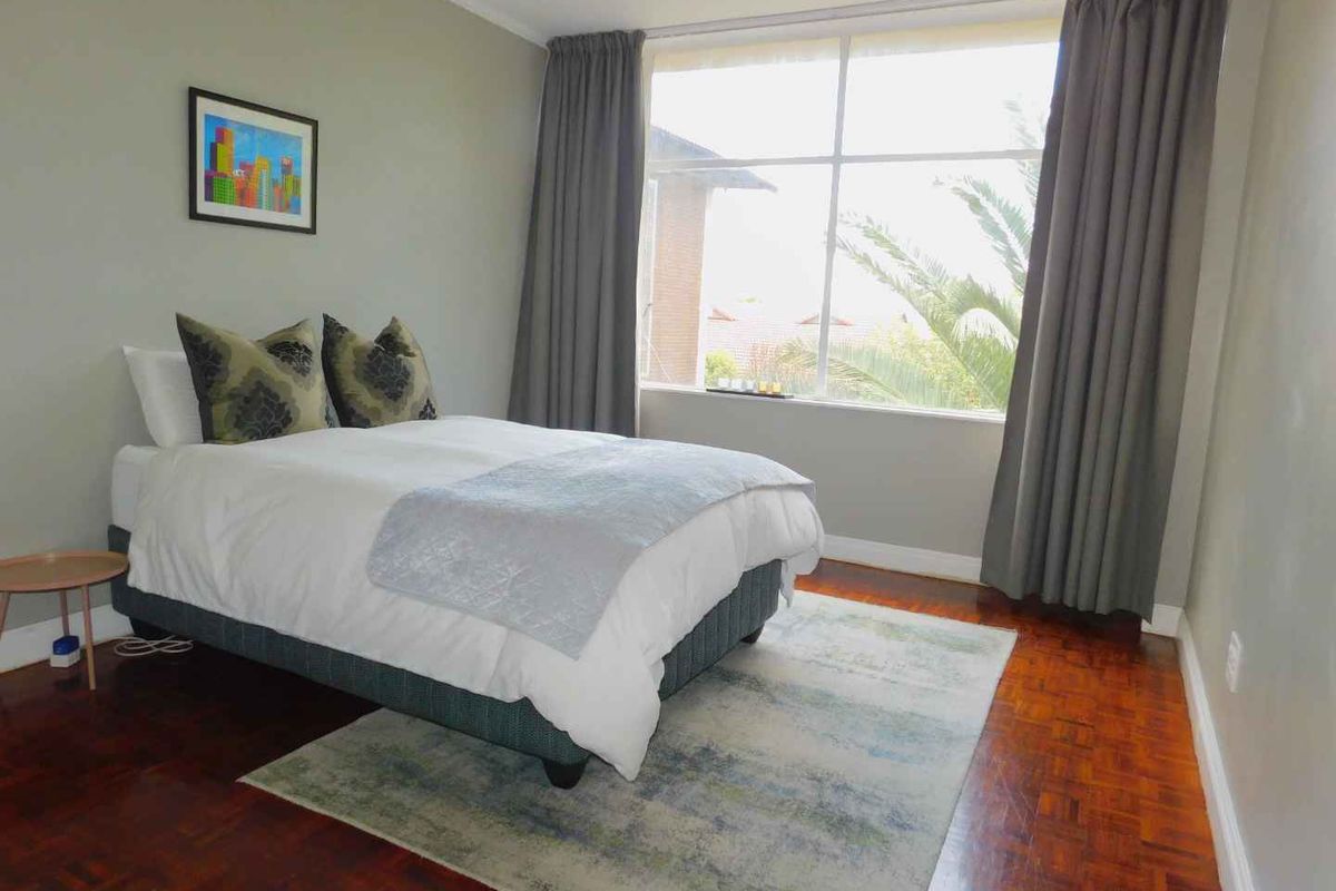 A well-lit bedroom featuring polished parquet flooring and a large window that provides natural light and views.