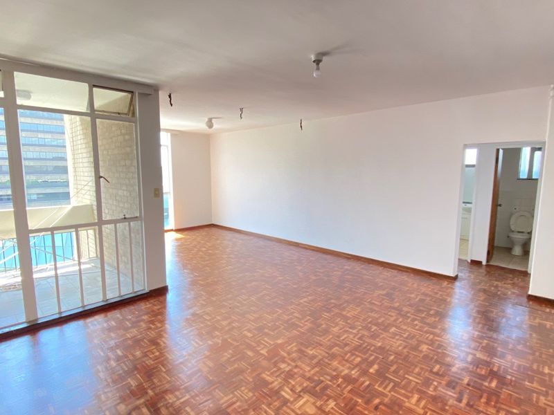 Spacious, empty living area featuring classic parquet flooring, large glass sliding doors leading to a balcony, and direct access to an adjacent bathroom.