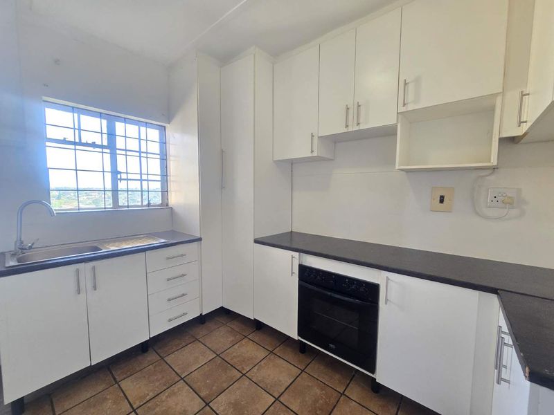 A functional kitchen featuring white built-in cabinetry, dark laminate countertops, a built-in oven, and tiled flooring with a window view.