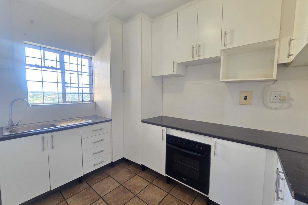 A functional kitchen featuring white built-in cabinetry, dark laminate countertops, a built-in oven, and tiled flooring with a window view.