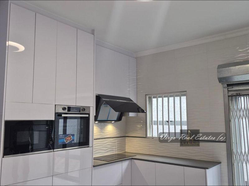 Modern kitchen featuring high-gloss white cabinetry, integrated appliances, sleek hob, extractor fan, and textured wall tiling.