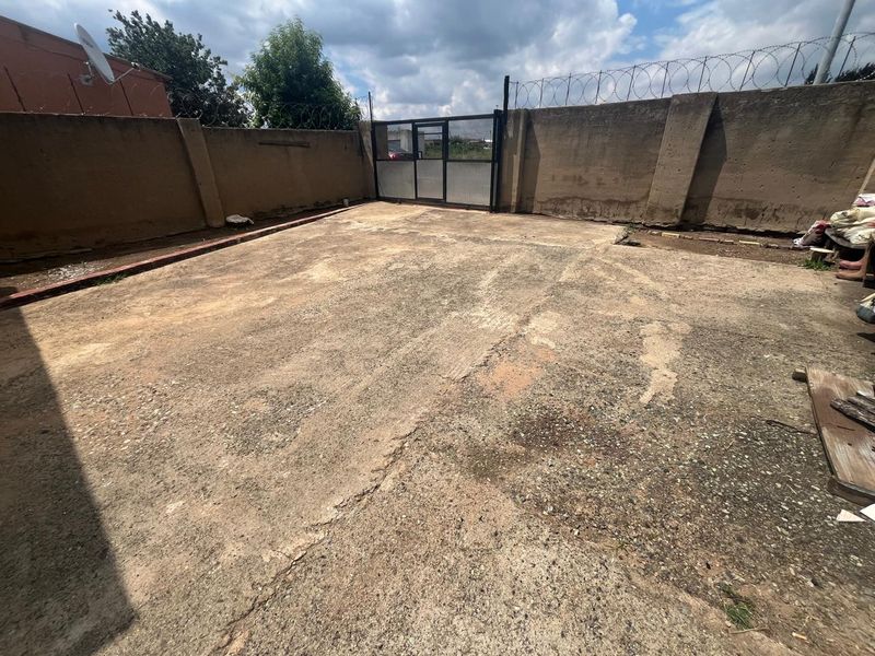 A paved rear courtyard area enclosed by a high perimeter wall with security razor wire and a metal access gate.
