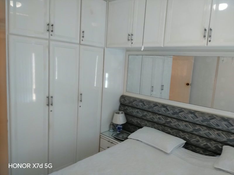 A bedroom featuring extensive white built-in cupboards, a large horizontal wall mirror, and a padded headboard.
