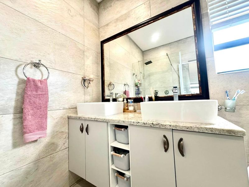 Modern bathroom featuring a double vanity with stone countertop, vessel sinks, large framed mirror, and a tiled shower enclosure.