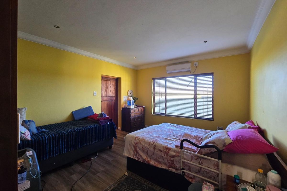A spacious bedroom featuring laminate flooring, recessed downlighting, and a wall-mounted air conditioning unit, offering a functional and comfortable living space.