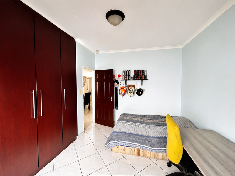 A bedroom featuring tiled flooring, built-in dark wood cupboards, and a ceiling light fixture, offering a functional space with neutral wall finishes.