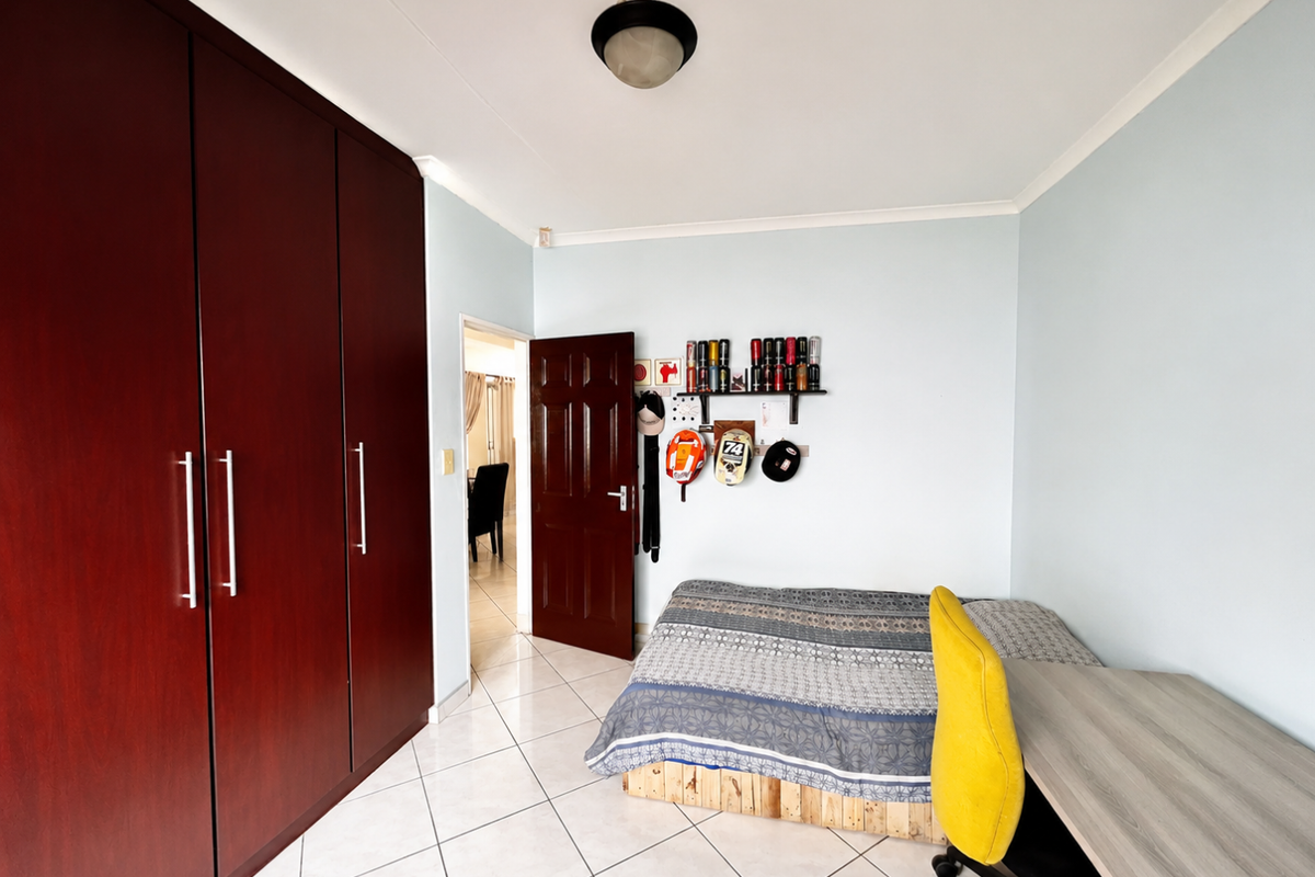 A bedroom featuring tiled flooring, built-in dark wood cupboards, and a ceiling light fixture, offering a functional space with neutral wall finishes.