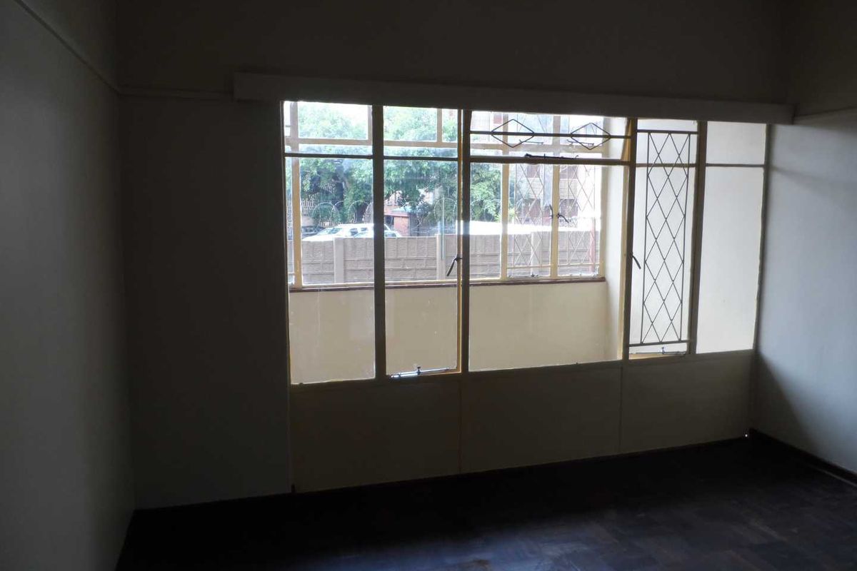 An empty bedroom featuring original parquet flooring and large steel-framed windows with security bars, offering a blank canvas for renovation.