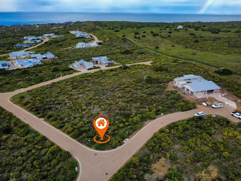 An aerial view of a vacant residential plot situated in a coastal estate, featuring paved road access and surrounding natural vegetation.