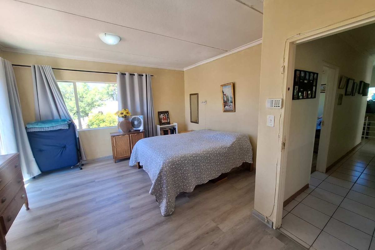 A spacious bedroom featuring light-toned laminate flooring and a large window, providing a functional living space with potential for cosmetic updates.