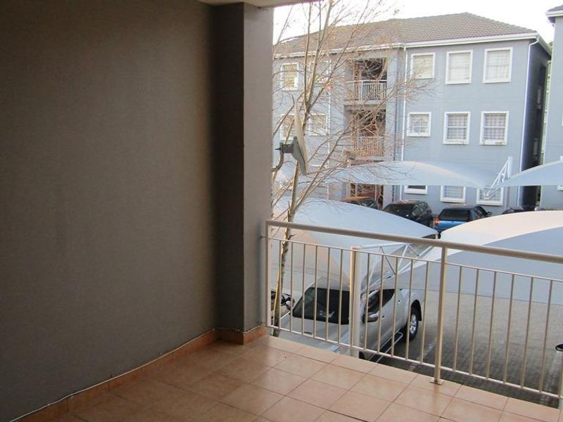 A covered balcony featuring tiled flooring and a metal balustrade, overlooking the apartment complex parking area.