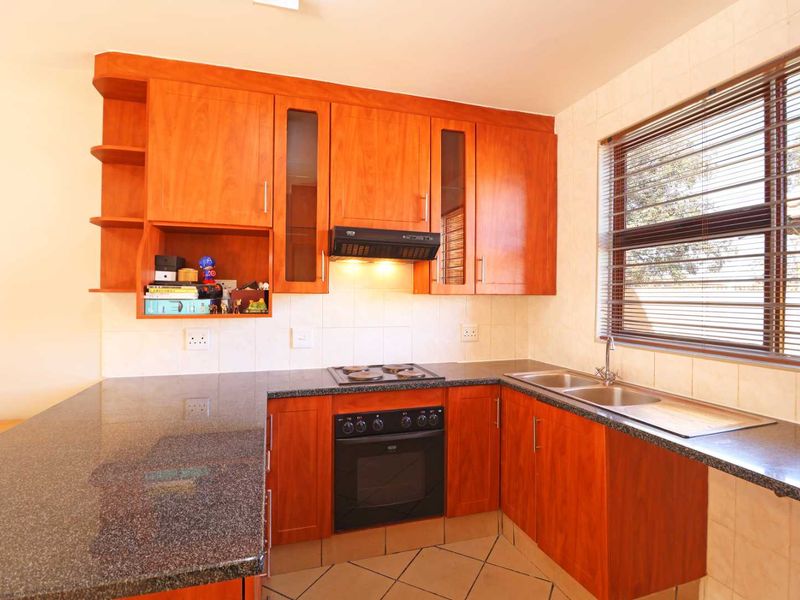 A functional kitchen featuring warm-toned wooden cabinetry, granite countertops, a built-in oven with hob, and a double basin sink with tiled backsplash.