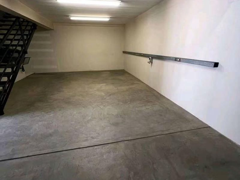 A clean, empty garage space featuring a concrete floor, fluorescent lighting, and an integrated metal staircase leading to an upper level.