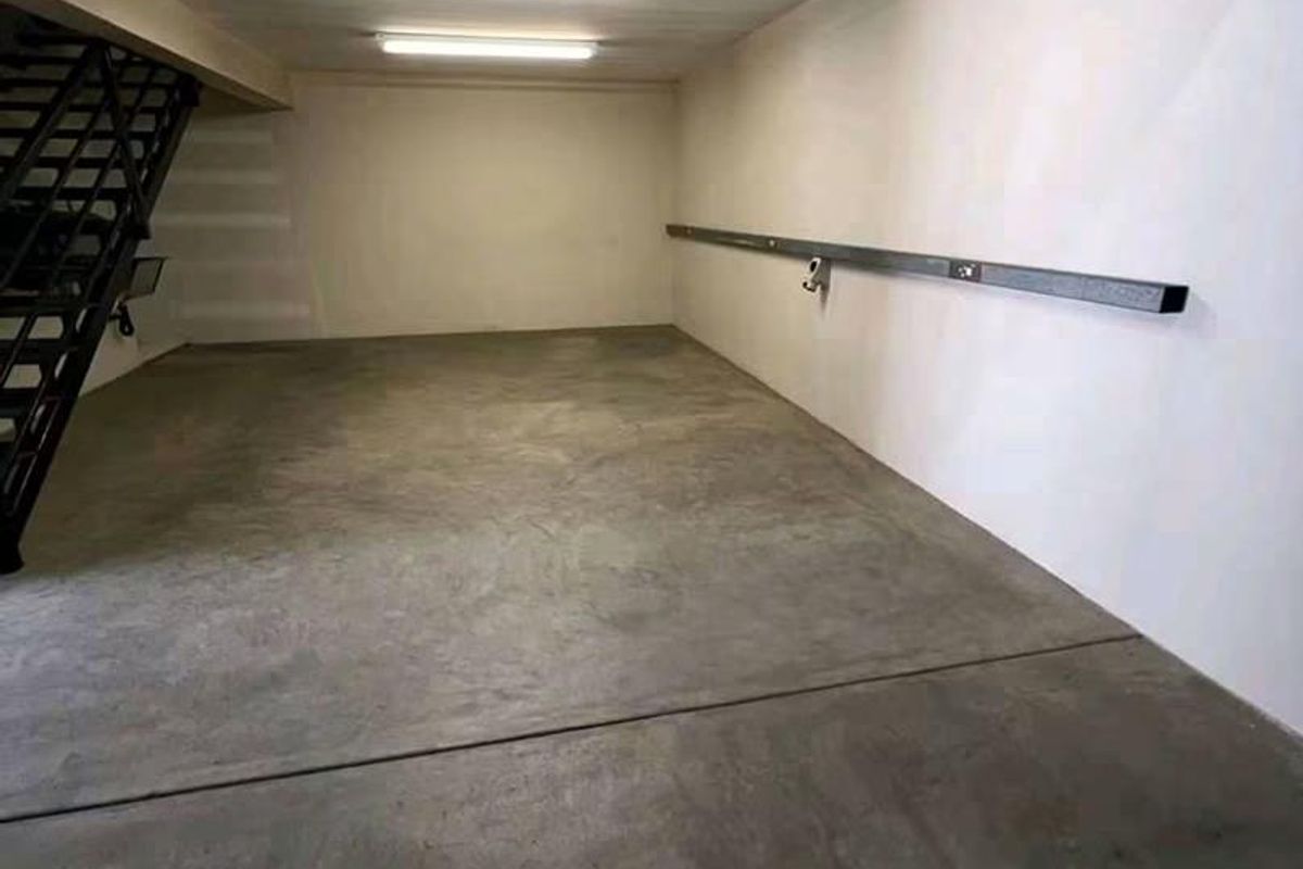 A clean, empty garage space featuring a concrete floor, fluorescent lighting, and an integrated metal staircase leading to an upper level.