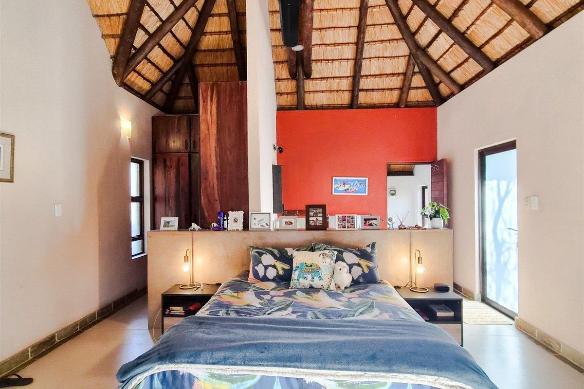 Spacious bedroom featuring a high vaulted thatched ceiling, exposed timber beams, and a central partition wall with integrated storage.