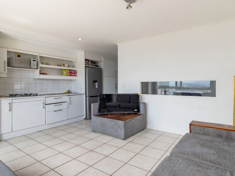 Open-plan living area featuring a functional kitchen with white cabinetry, gas hob, tiled flooring, and a unique horizontal window offering natural light.