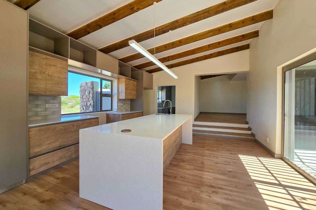 Modern kitchen featuring a large central island with stone countertop, wood-finish cabinetry, exposed timber ceiling beams, and direct access to outdoor areas.