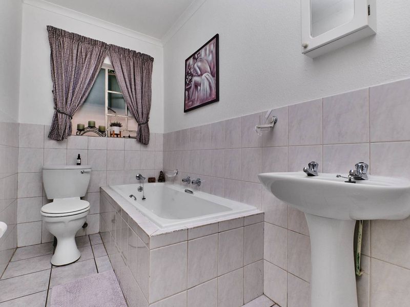 A functional bathroom featuring a pedestal basin, built-in bathtub, and toilet with neutral wall and floor tiling.