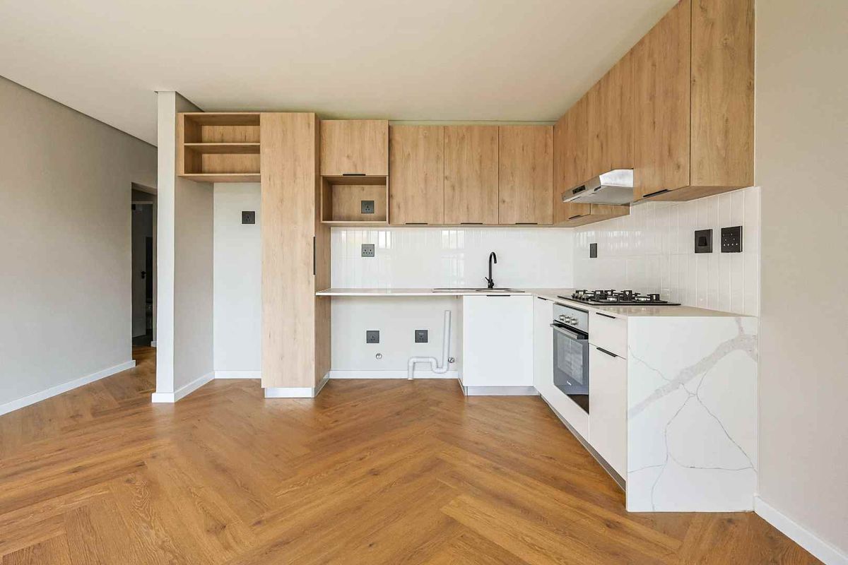 Modern kitchen featuring light wood cabinetry, stone countertops, herringbone flooring, and integrated appliances including an oven and gas hob.