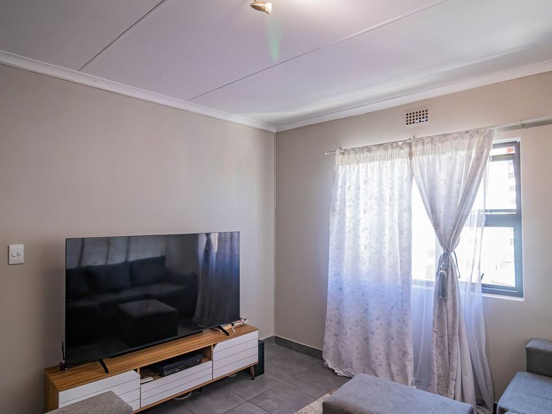 A living room featuring tiled flooring, neutral wall paint, and a window with natural light, providing a functional and comfortable living space.