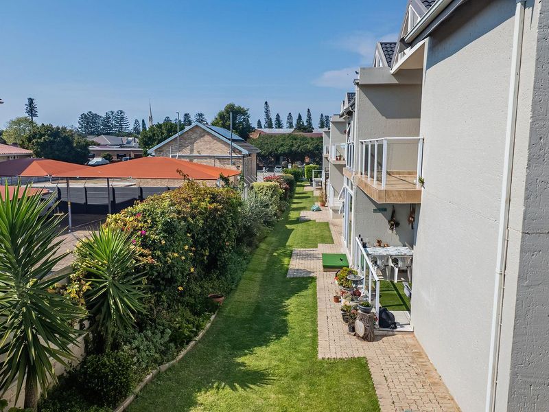 An elevated view of the rear exterior of the apartment complex, featuring a landscaped garden, paved walkways, and private balconies.