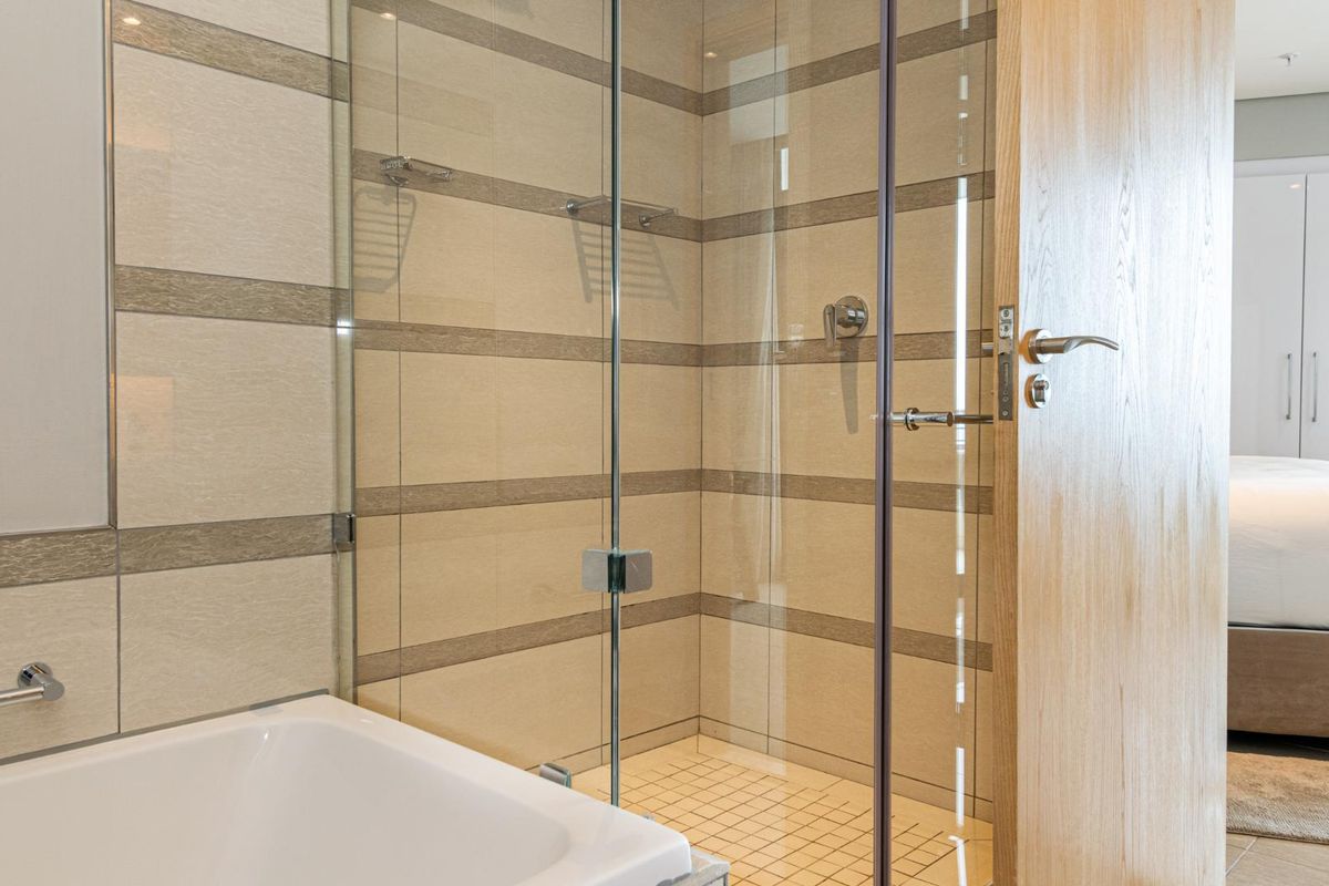 Modern bathroom featuring a glass-enclosed shower, tiled walls with horizontal accents, and a built-in bathtub, adjacent to a bedroom area.