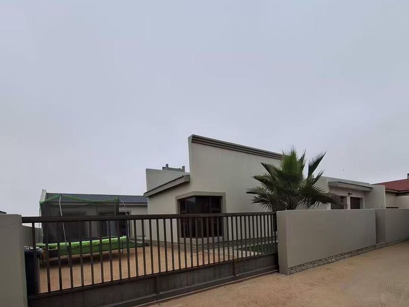 Front view of a modern house featuring a secure sliding gate, perimeter boundary wall, and a paved driveway area.