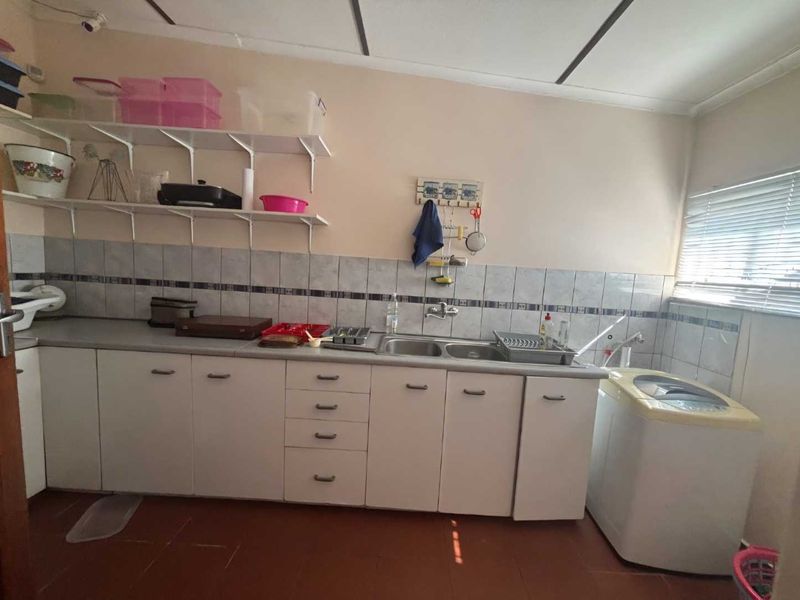 Functional laundry area featuring built-in cabinetry, double basin sink, tiled splashback, and wall-mounted shelving for storage.