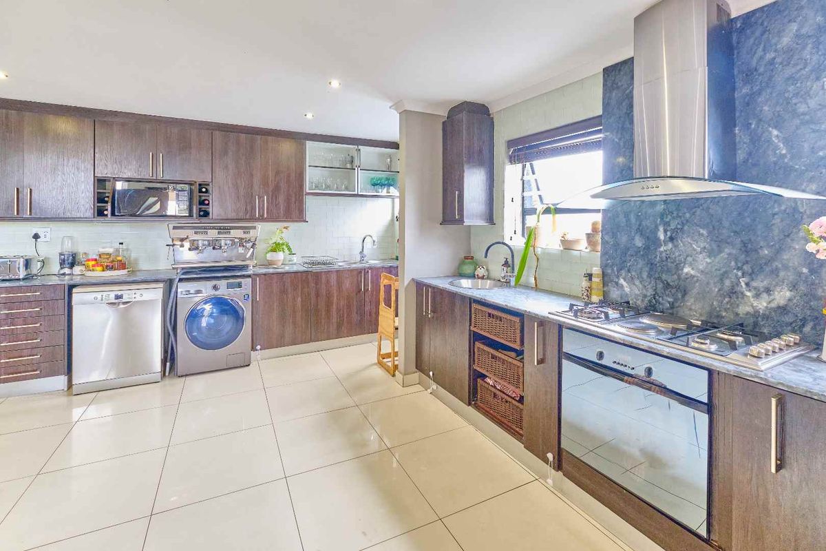 Spacious kitchen featuring dark wood cabinetry, gas hob, stainless steel extractor, built-in oven, and tiled flooring with ample counter space.