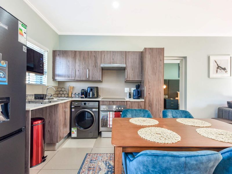 Modern open-plan kitchen featuring wood-grain cabinetry, integrated appliances, and tiled flooring, seamlessly flowing into the dining and living area.