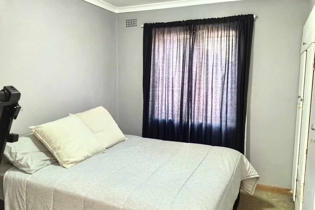 A standard bedroom featuring neutral grey walls, built-in wardrobe storage, and a window with curtain fixtures.