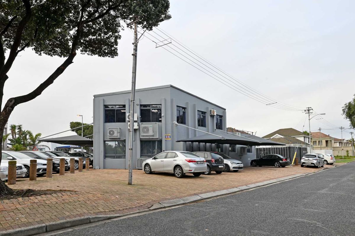 Exterior view of a commercial mixed-use building featuring a paved parking area, shade sail structures, and wall-mounted air conditioning units.