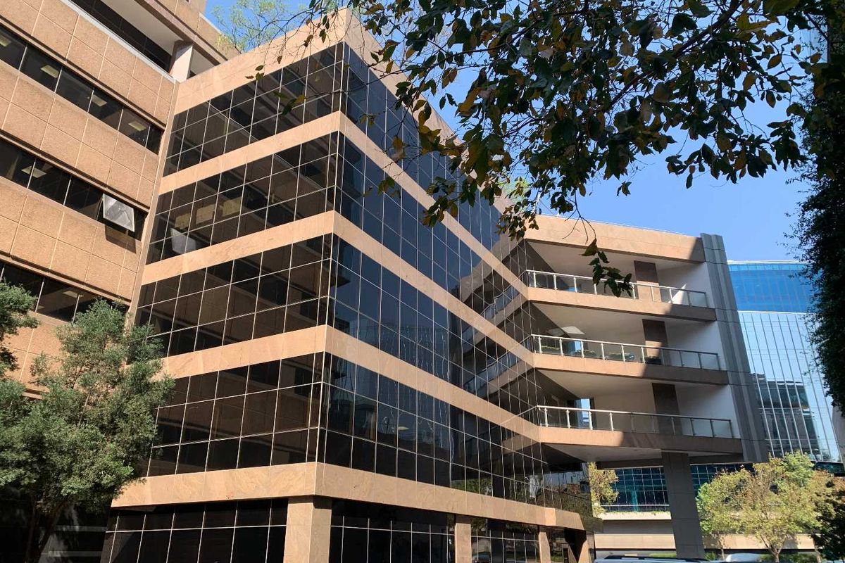 A modern multi-story office building featuring a glass curtain wall facade, stone cladding, and integrated balconies with metal railings.