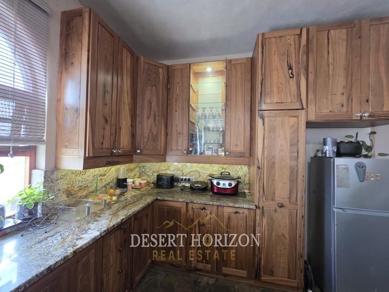 A well-maintained kitchen featuring rich wooden cabinetry, granite countertops, a stone backsplash, and integrated glass-front display shelving with accent lighting.