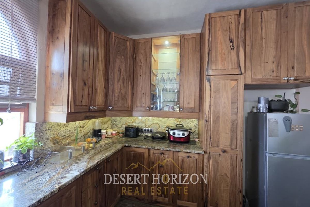 A well-maintained kitchen featuring rich wooden cabinetry, granite countertops, a stone backsplash, and integrated glass-front display shelving with accent lighting.