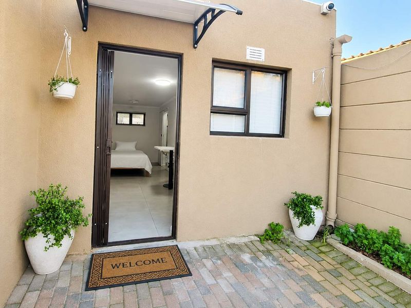 A neat rear exterior view of the cottage featuring brick paving, a sliding door entrance, and a secure boundary wall.