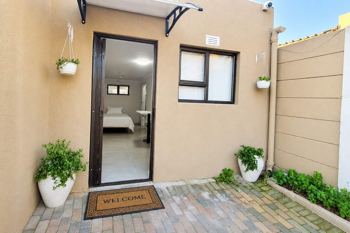 A neat rear exterior view of the cottage featuring brick paving, a sliding door entrance, and a secure boundary wall.